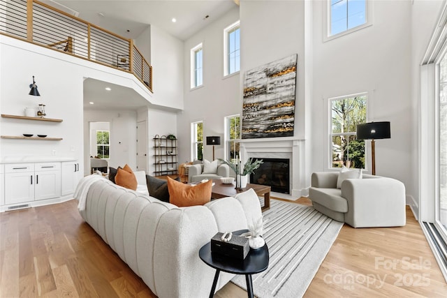 living room with light wood-style flooring, a towering ceiling, and a wealth of natural light