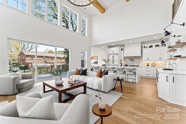 living room with beam ceiling, recessed lighting, a chandelier, a high ceiling, and light wood-style floors