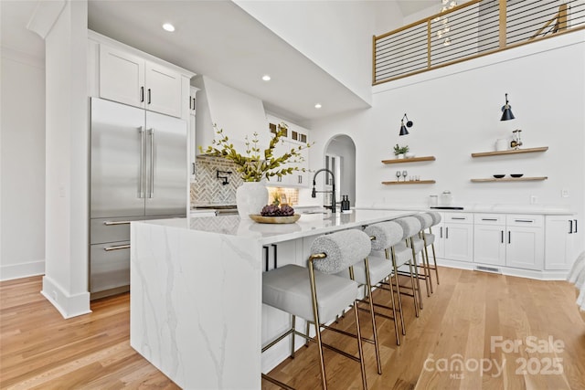 kitchen with stainless steel built in fridge, a sink, open shelves, light wood-type flooring, and arched walkways