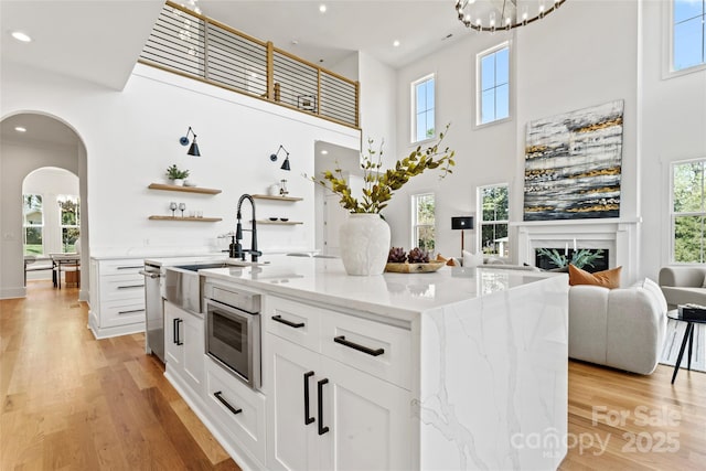 kitchen with white cabinetry, open shelves, arched walkways, a fireplace, and light wood-type flooring