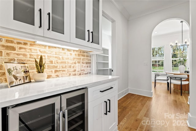 bar featuring a bar, beverage cooler, baseboards, light wood finished floors, and crown molding