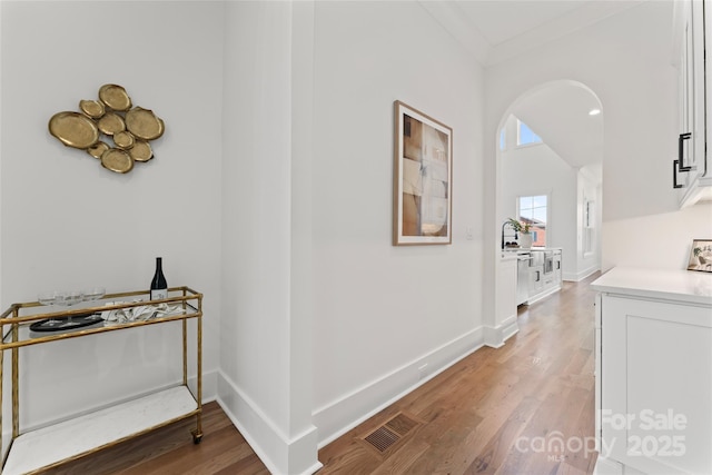hallway featuring light wood finished floors, arched walkways, baseboards, and visible vents