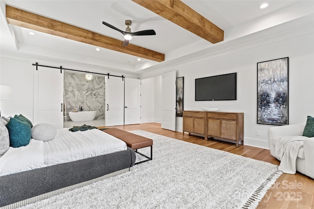 bedroom featuring wood finished floors, beam ceiling, a barn door, recessed lighting, and baseboards