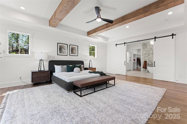 bedroom with beamed ceiling, a barn door, light wood-type flooring, and recessed lighting