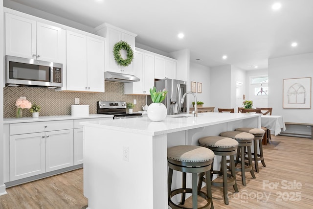 kitchen featuring a kitchen bar, under cabinet range hood, a sink, an island with sink, and appliances with stainless steel finishes