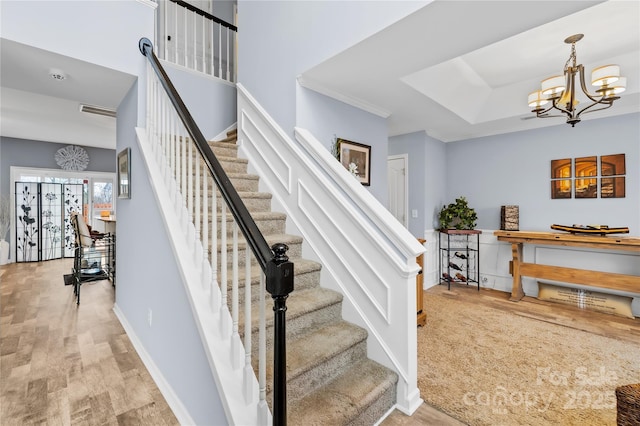 stairway with wood finished floors, visible vents, baseboards, a tray ceiling, and a chandelier