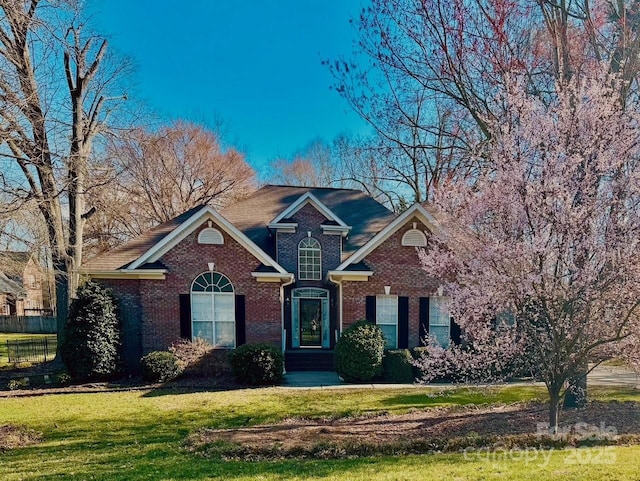 traditional-style home with brick siding, a front lawn, and fence