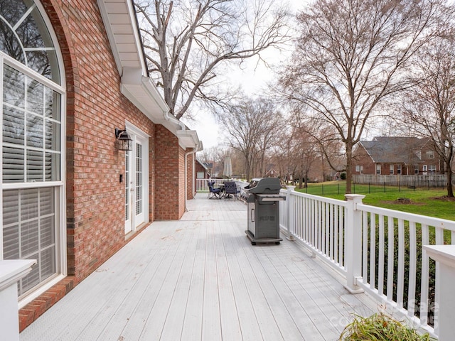 deck featuring outdoor dining space, fence, a lawn, a residential view, and a grill