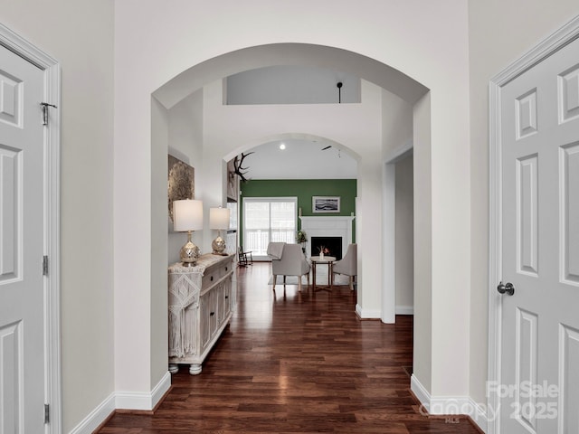 hall with dark wood finished floors, arched walkways, and baseboards