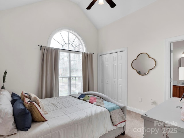 carpeted bedroom with a closet, baseboards, high vaulted ceiling, and a ceiling fan