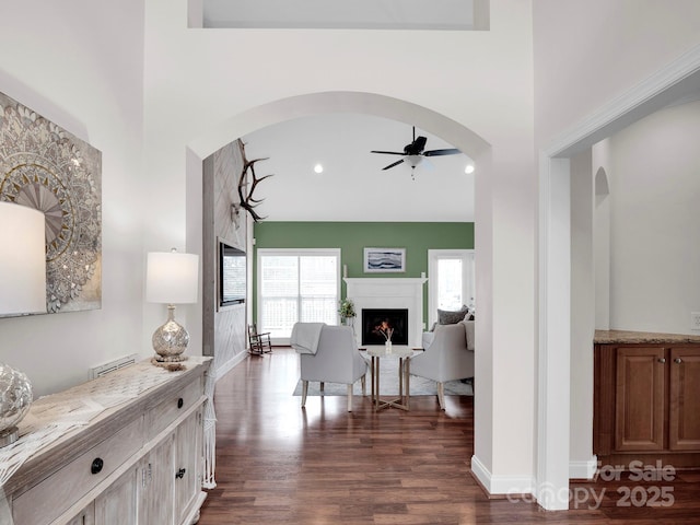 hallway featuring baseboards, dark wood finished floors, recessed lighting, a high ceiling, and arched walkways