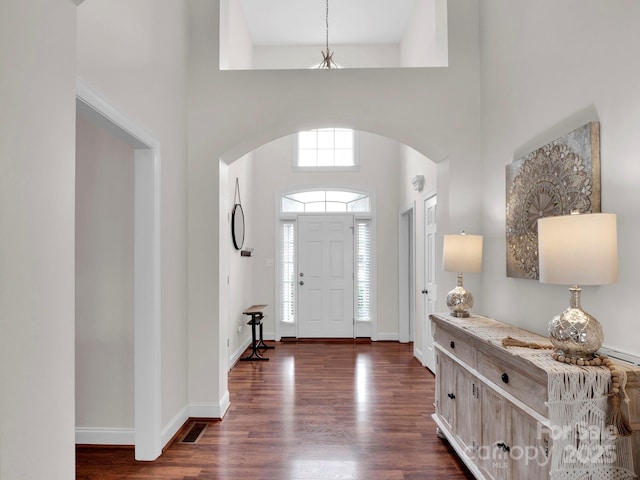 foyer featuring arched walkways, dark wood finished floors, and baseboards