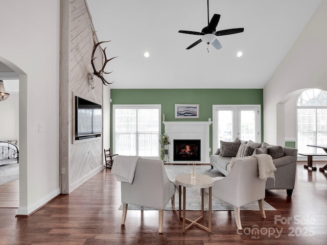 living room featuring arched walkways, high vaulted ceiling, and a warm lit fireplace