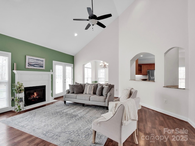 living area with a high end fireplace, baseboards, ceiling fan with notable chandelier, arched walkways, and dark wood-style floors