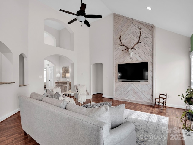 living room with dark wood-style floors, ceiling fan, arched walkways, and baseboards