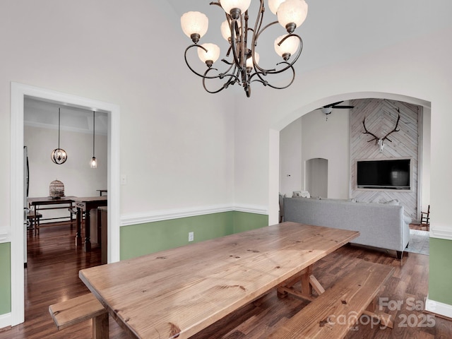 dining area with arched walkways, an inviting chandelier, and wood finished floors