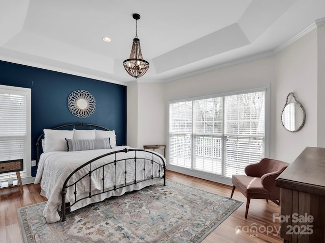 bedroom featuring a notable chandelier, a raised ceiling, and wood finished floors