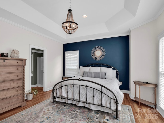 bedroom with a tray ceiling, wood finished floors, multiple windows, and a chandelier