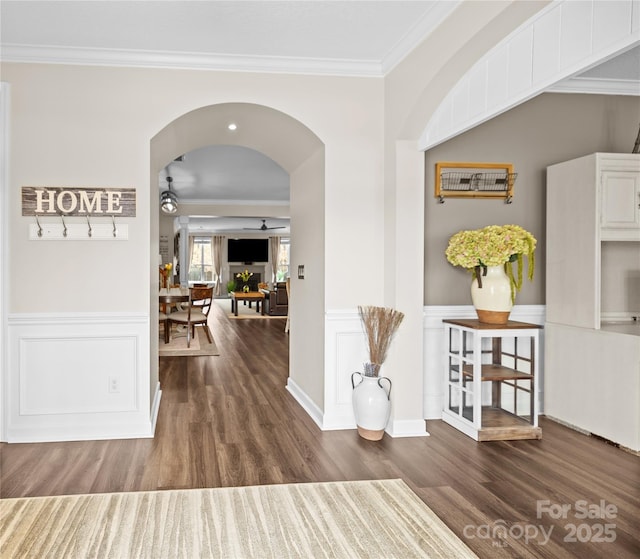 hallway featuring arched walkways, wainscoting, crown molding, and wood finished floors