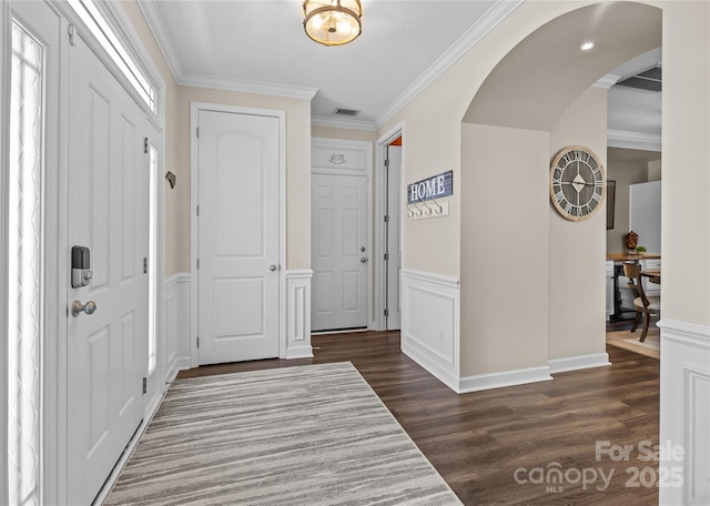 entryway with crown molding, arched walkways, visible vents, and dark wood-style flooring