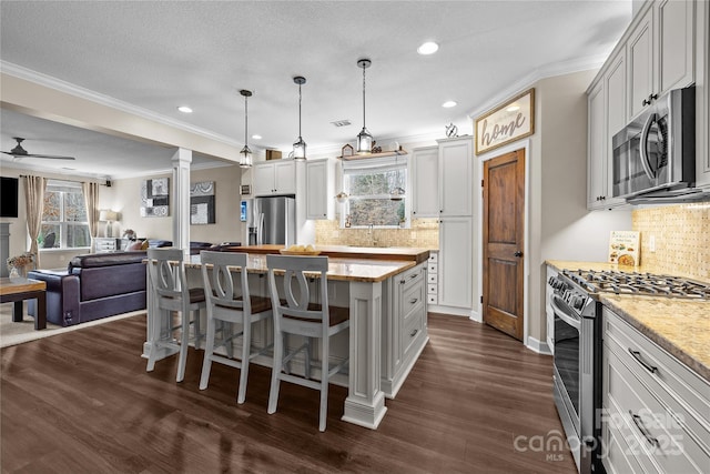 kitchen featuring dark wood finished floors, decorative columns, stainless steel appliances, open floor plan, and a center island