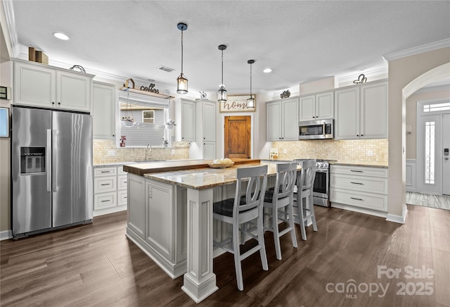 kitchen with a kitchen island, arched walkways, a sink, stainless steel appliances, and crown molding