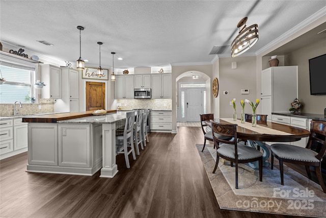 kitchen featuring stainless steel microwave, visible vents, a center island, dark wood-type flooring, and arched walkways