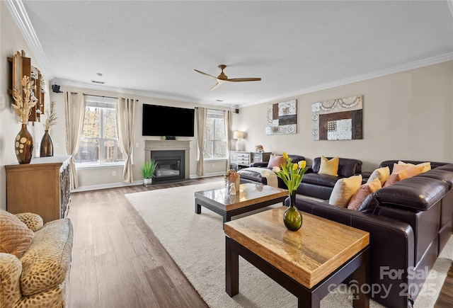 living area featuring a wealth of natural light, a fireplace with flush hearth, crown molding, and wood finished floors