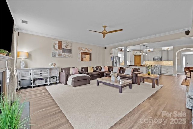 living room with arched walkways, visible vents, crown molding, and light wood-style floors