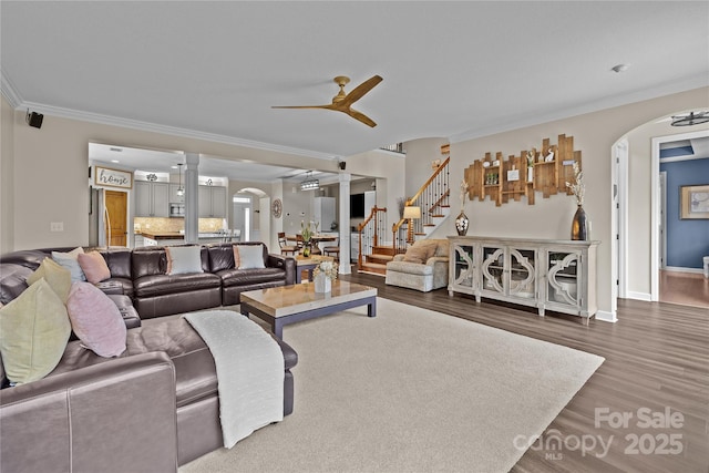 living area with stairway, arched walkways, ceiling fan, and crown molding