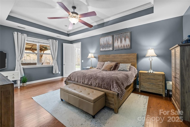 bedroom with wood finished floors, visible vents, baseboards, ceiling fan, and a raised ceiling