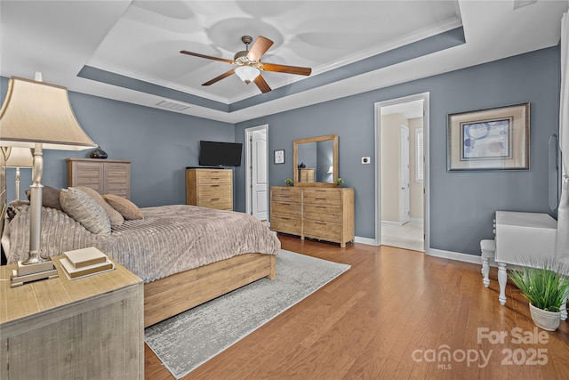 bedroom featuring baseboards, a tray ceiling, wood-type flooring, and visible vents