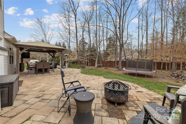 view of patio / terrace with outdoor dining space, an outdoor fire pit, a fenced backyard, a gazebo, and a trampoline