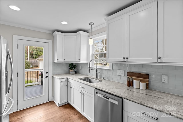 kitchen with light wood finished floors, ornamental molding, a sink, appliances with stainless steel finishes, and white cabinetry