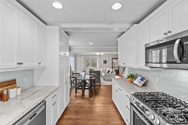 kitchen with wood finished floors, white cabinetry, stainless steel appliances, crown molding, and decorative backsplash