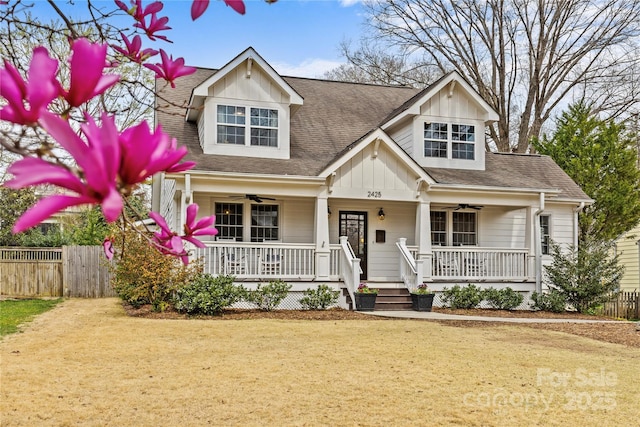 craftsman house with a ceiling fan, fence, covered porch, a front yard, and a shingled roof