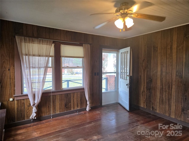 empty room featuring crown molding, baseboards, wood walls, wood finished floors, and a ceiling fan