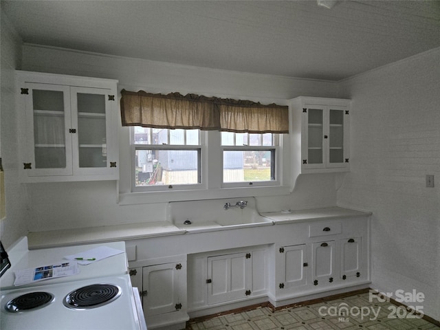 kitchen featuring glass insert cabinets, light countertops, white cabinets, white electric stove, and a sink