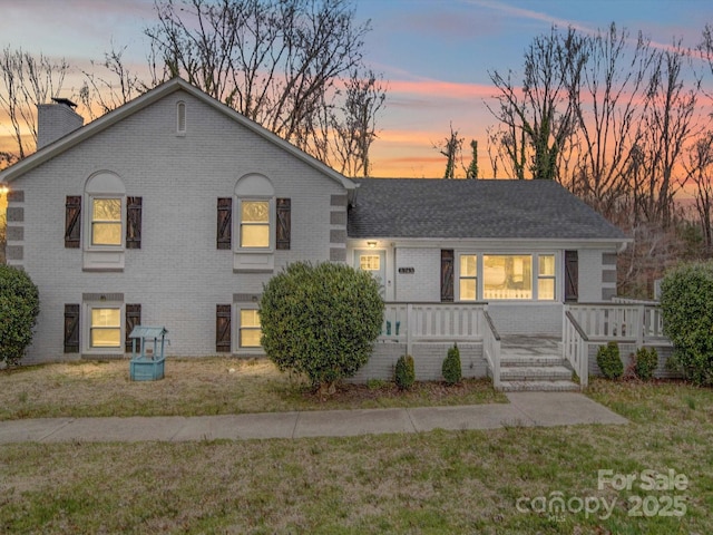 split level home with brick siding, a lawn, and a chimney