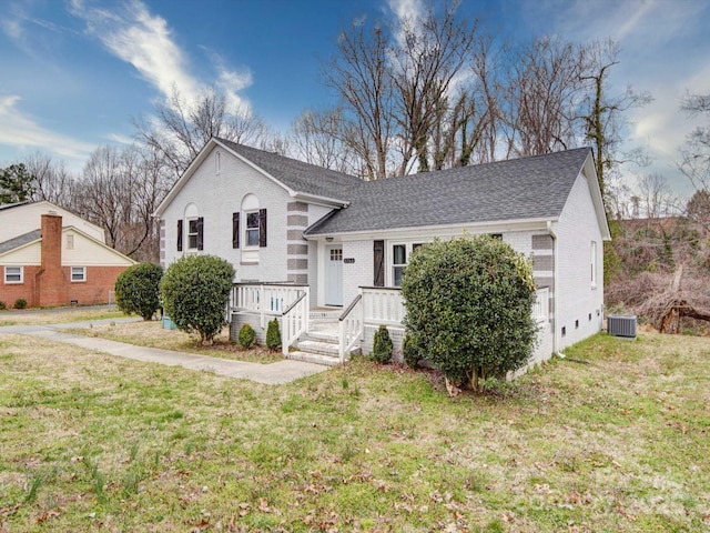 split level home with central AC, roof with shingles, a front yard, a wooden deck, and brick siding