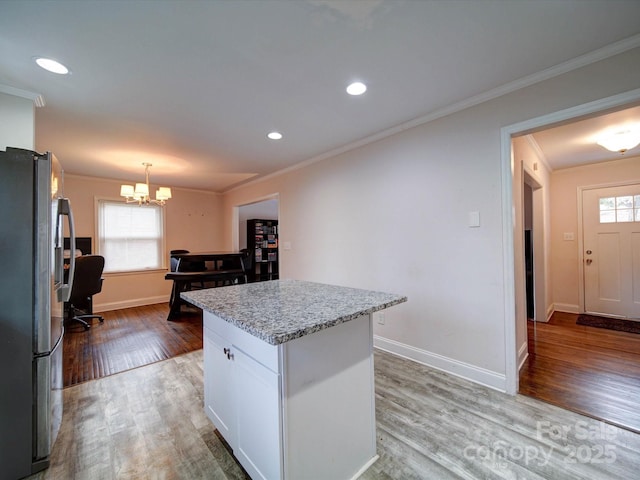 kitchen with ornamental molding, a kitchen island, stainless steel fridge, white cabinets, and light wood finished floors