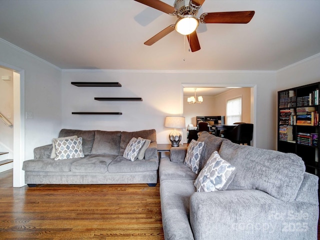 living area featuring stairway, ceiling fan with notable chandelier, crown molding, and wood finished floors