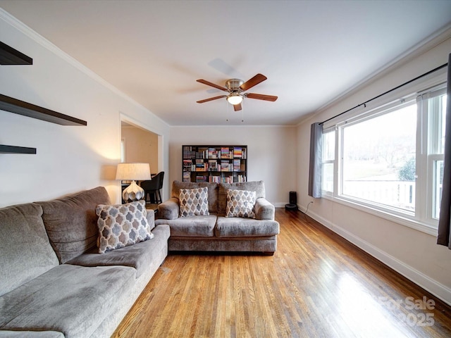 living room with crown molding, baseboards, light wood-type flooring, and a ceiling fan