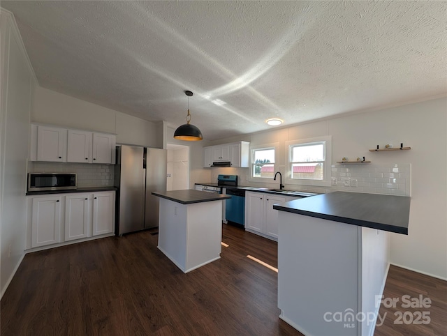 kitchen with dark countertops, a peninsula, stainless steel appliances, dark wood-style floors, and white cabinetry