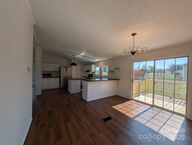 kitchen with a notable chandelier, dark countertops, dark wood-style floors, stainless steel appliances, and a peninsula