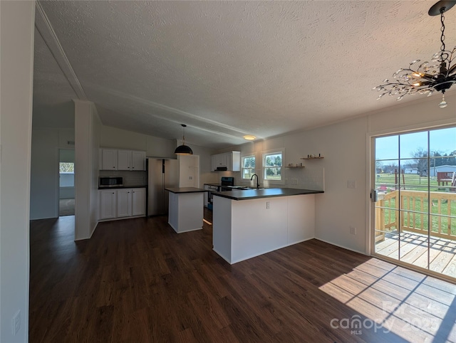 kitchen with dark wood-type flooring, dark countertops, stainless steel appliances, a peninsula, and lofted ceiling