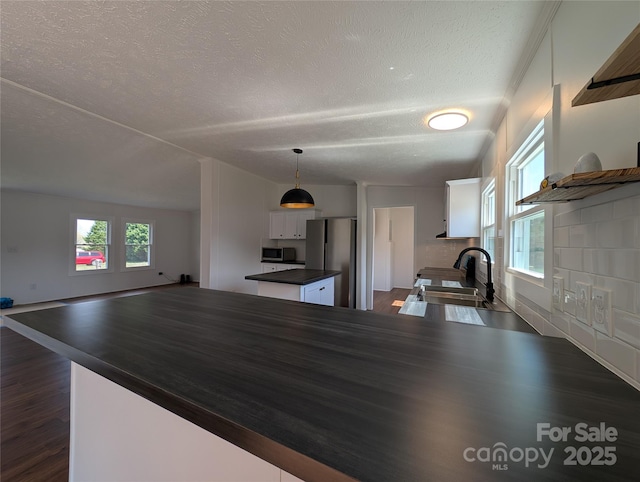 kitchen with dark countertops, dark wood finished floors, appliances with stainless steel finishes, white cabinetry, and a sink