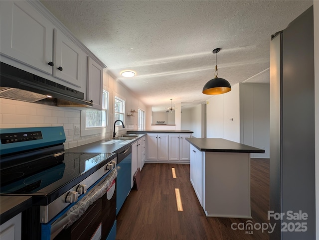 kitchen with dark countertops, under cabinet range hood, a peninsula, electric range, and a sink