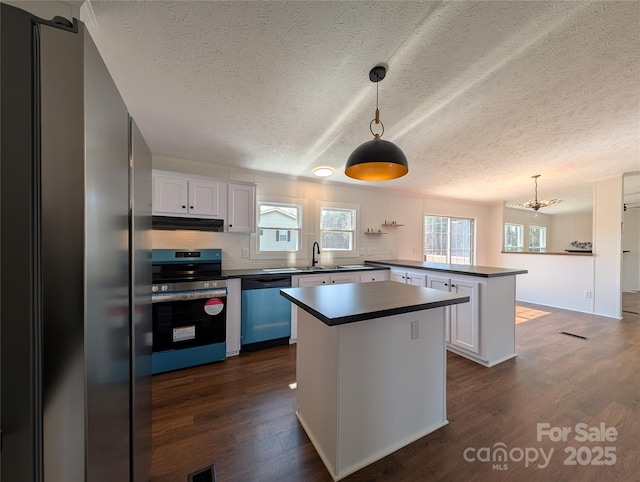 kitchen featuring dark countertops, under cabinet range hood, dark wood finished floors, appliances with stainless steel finishes, and a peninsula