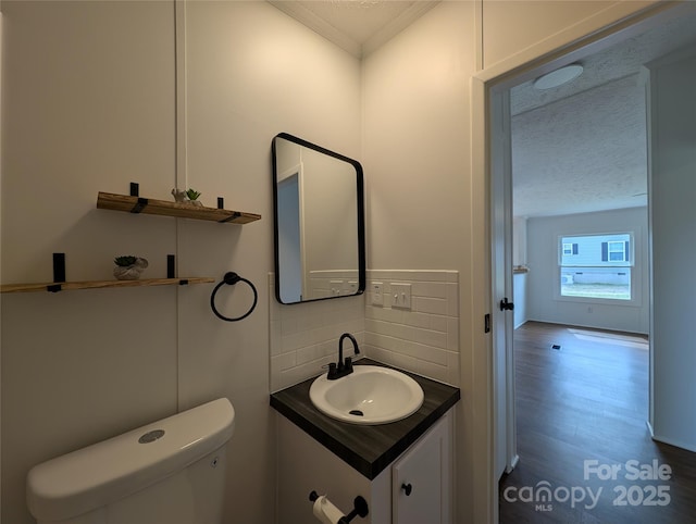 bathroom with toilet, a textured ceiling, tasteful backsplash, wood finished floors, and vanity